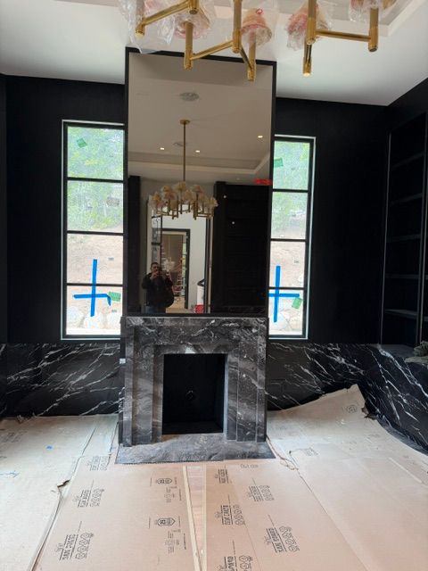 Black marble fireplace under a mirrored wall with tall windows and protective floor covering in a room under renovation