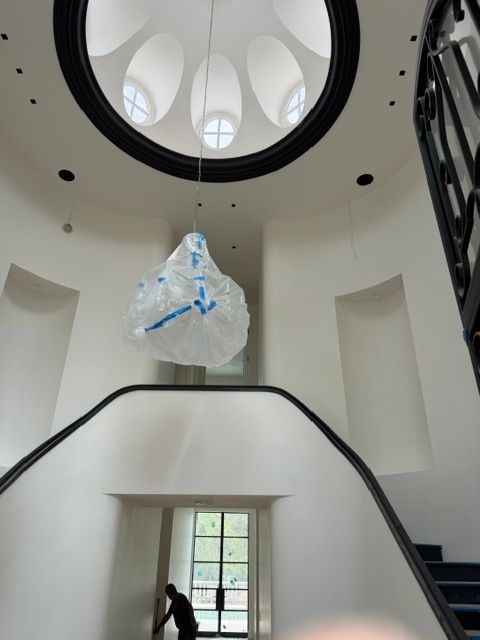 Large white atrium with skylight, hanging wrapped object, and staircase along the side.