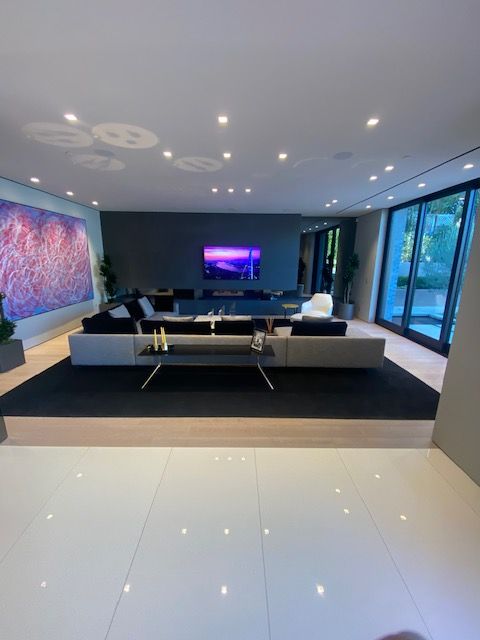 Modern living room with a large sectional sofa, TV, glossy tile floor, and floor-to-ceiling windows