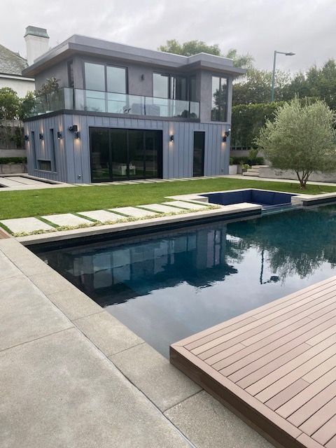 Modern two-story house with glass balcony and a backyard pool beside a wooden deck