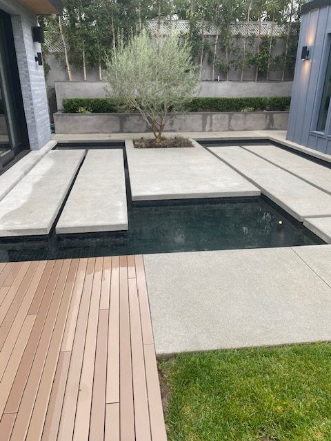 Modern courtyard with raised concrete platforms, a narrow water feature, and wood and stone decking
