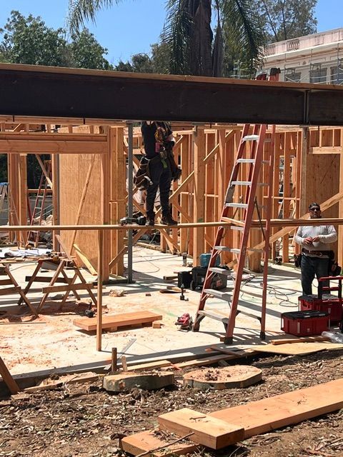 Construction workers framing a wooden building, with ladders, lumber, and tools on site