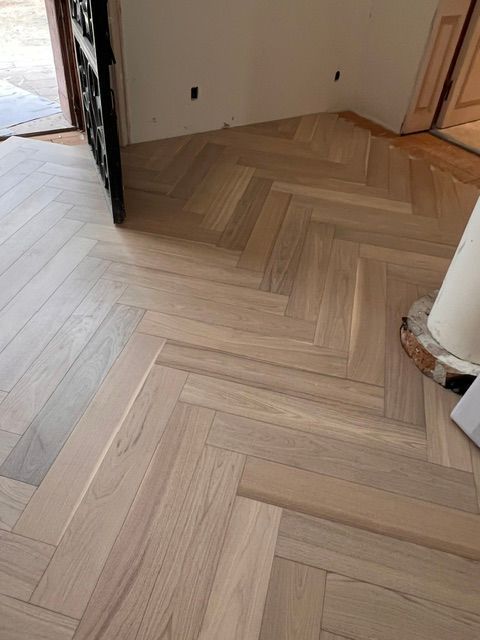 Light wood herringbone floor in a room corner with white walls and an open doorway