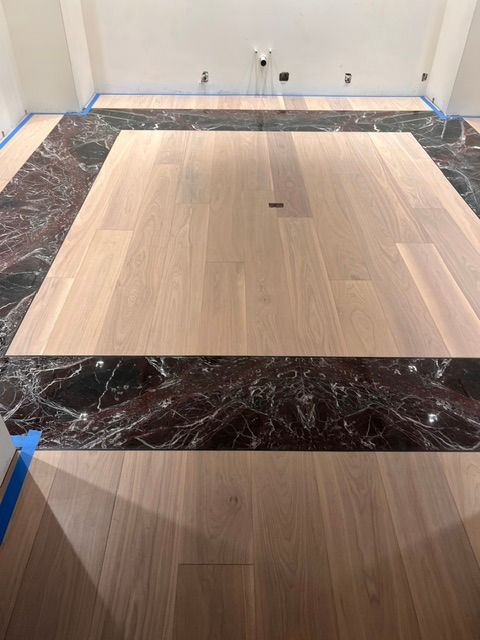 Empty room with unfinished flooring, showing light wood center panels and dark marble border trim.