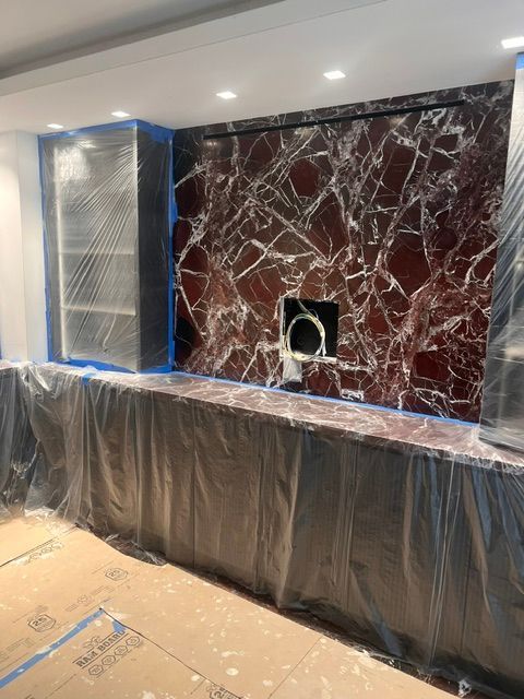 Marble wall panel installation in progress, with protective plastic covering the lower cabinets and floor.