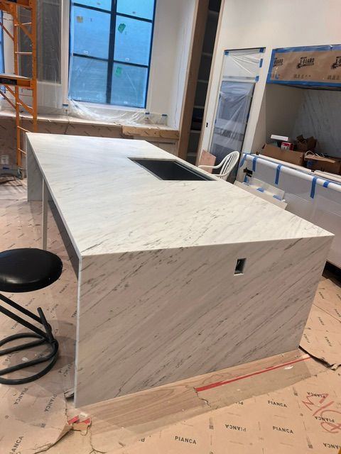 White rectangular kitchen island under construction in a room with large windows and scaffolding tools nearby