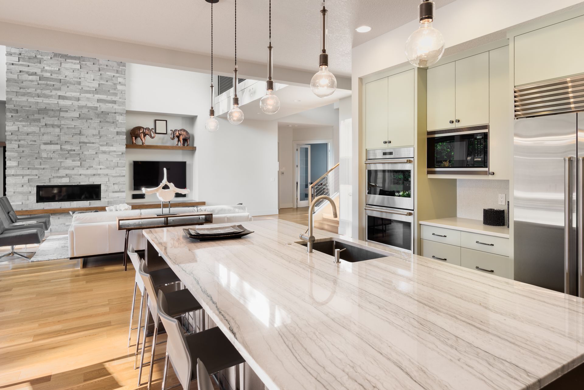 Modern open-concept kitchen with marble island, stainless appliances, pendant lights, and stone fireplace seating area