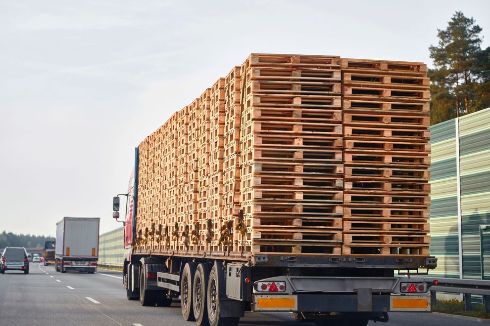 Un semirimorchio carico di un'alta e fitta pila di pallet di legno che percorre un'autostrada.