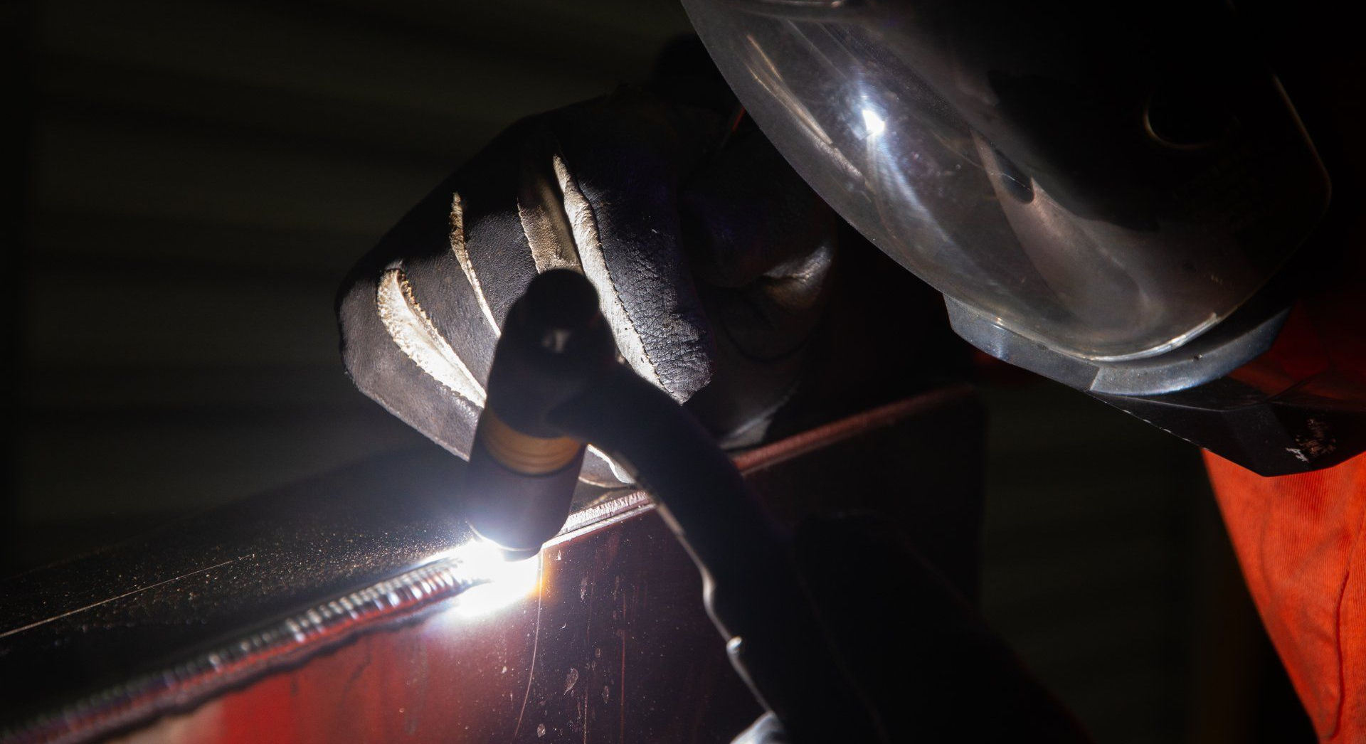 Welder In Protective Gear Working At Metal Table