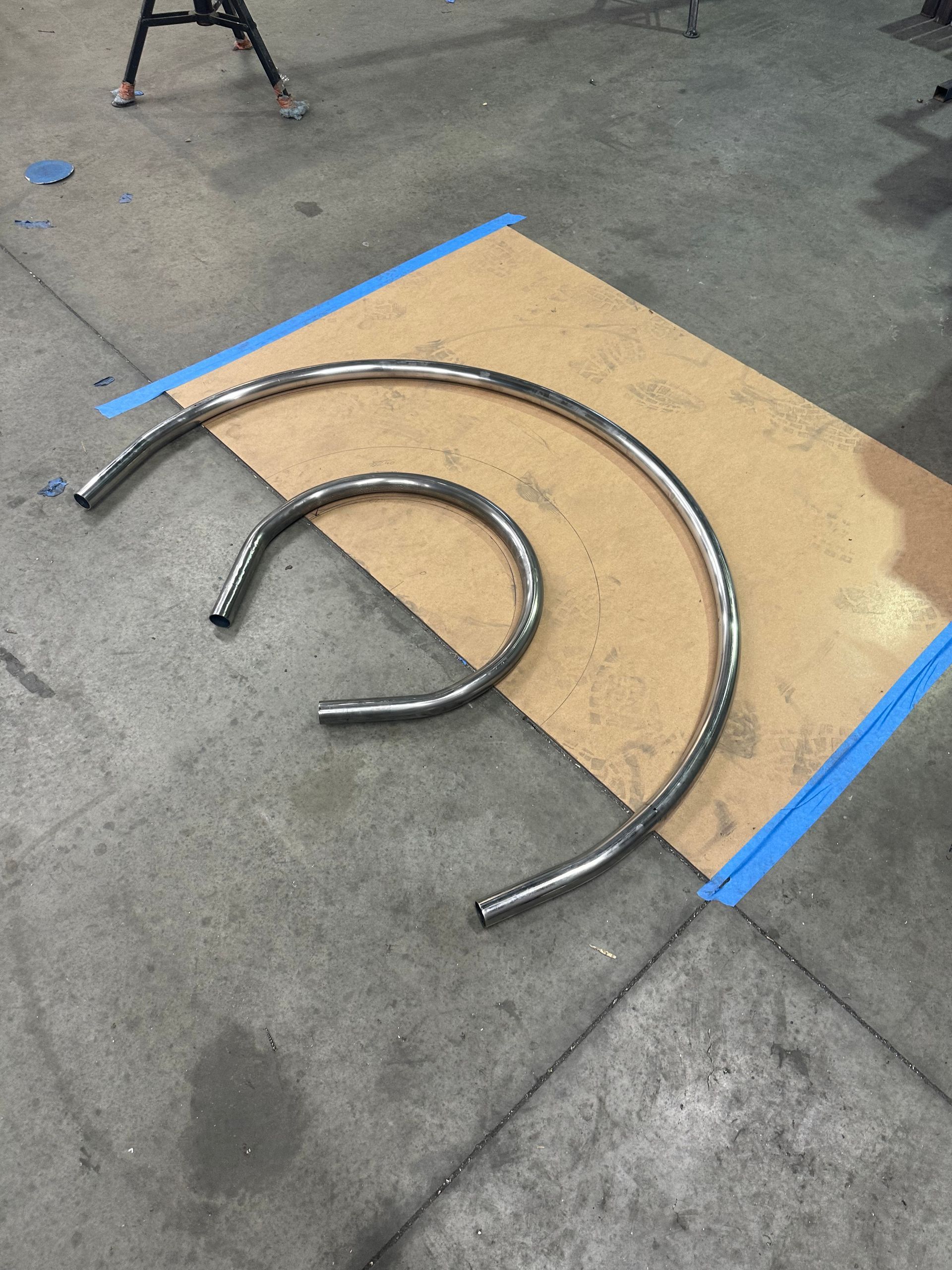 Two Bent Metal Tubes on Cardboard, Taped to A Concrete Floor — EB Metalworks in Newcastle, NSW