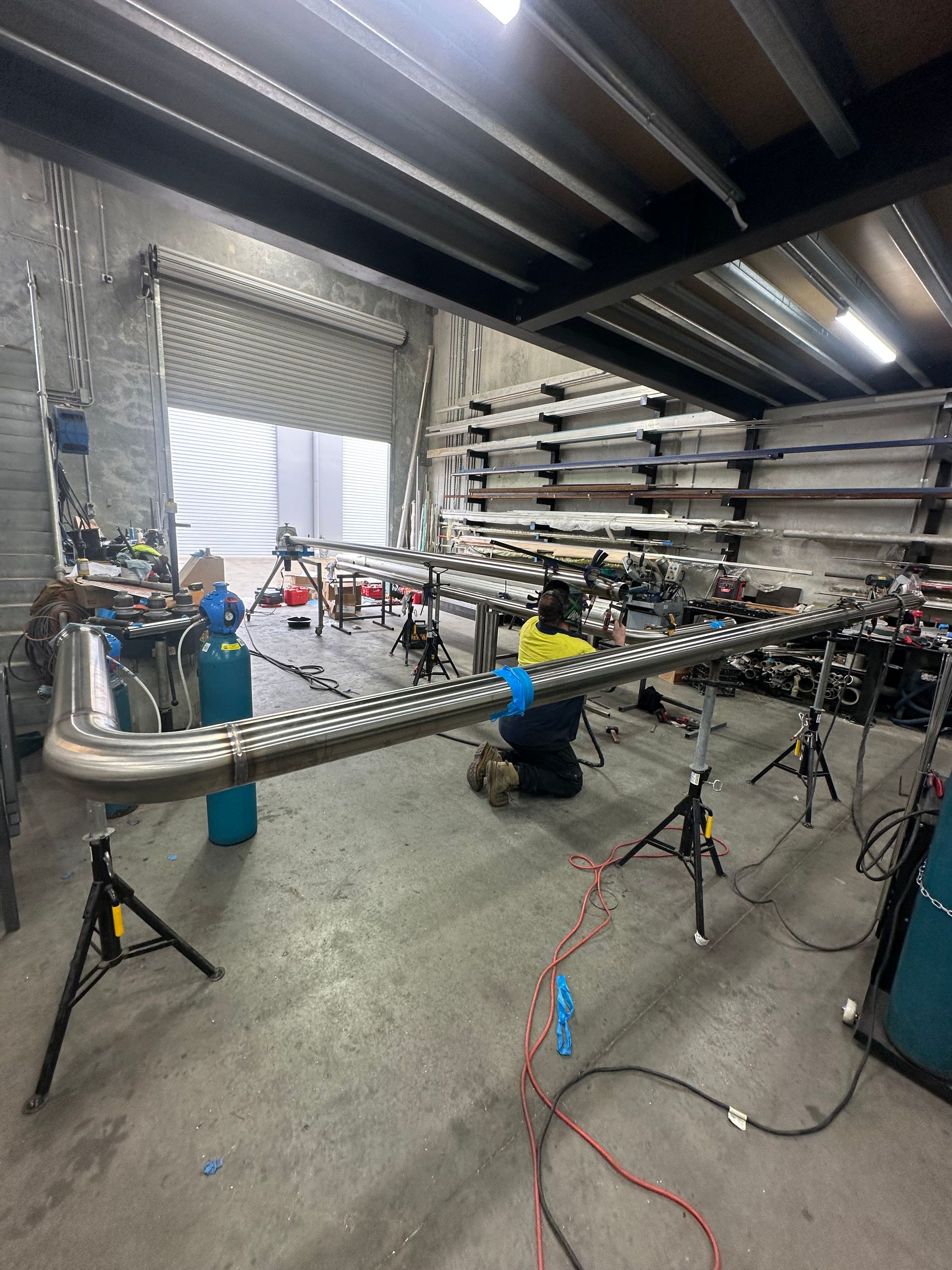 Warehouse Workshop with Long Metal Beams on Tripods, Tools, Cables, and Shelving — EB Metalworks in Sydney, NSW