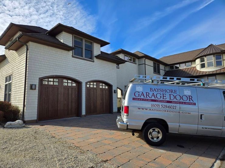 A work van parked in the driveway of a house with two wooden arched garage doors.