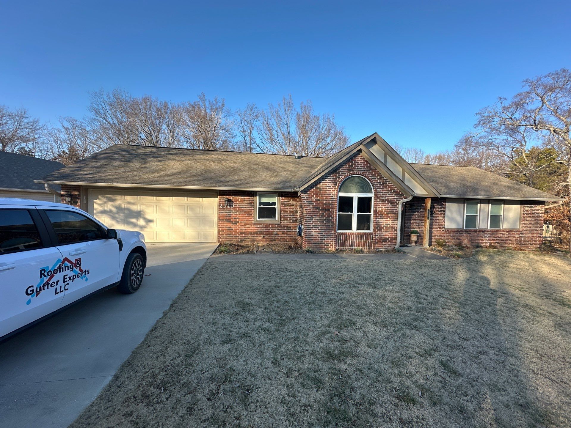 Suburban brick house with a driveway, winter lawn, and a white van parked at left