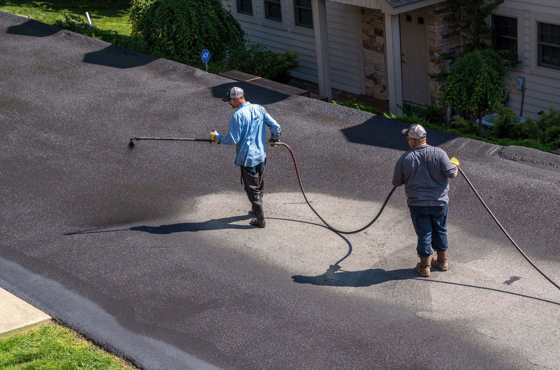 Two people washing a driveway with pressure washers outside a house.