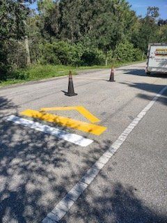 A yellow arrow is painted on the side of a road next to two traffic cones.