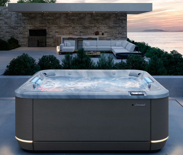 Jacuzzi sur une terrasse avec vue sur l'océan au coucher du soleil. Baignoire gris foncé à l'eau bouillonnante.
