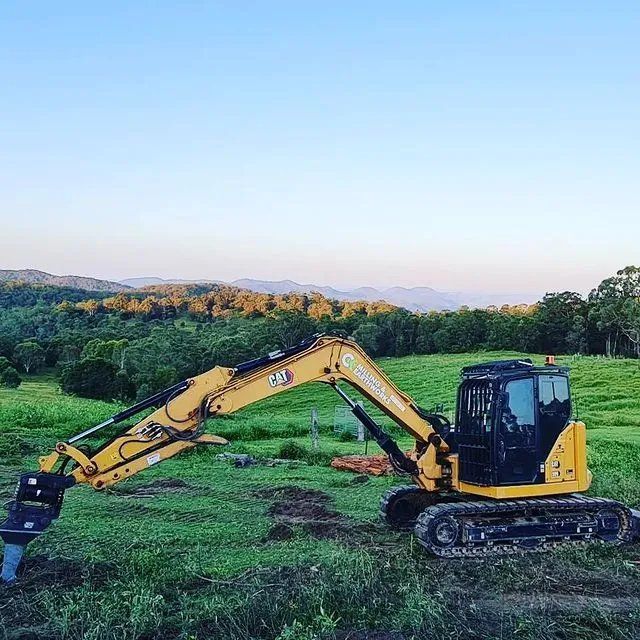 A Yellow Excavator Is Sitting in The Middle of A Grassy Field — CK's Milling & Earthworks in Noosa Heads, QLD