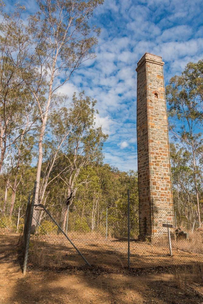 A Tall Stone Chimney Is Surrounded by Trees and A Fence — CK's Milling & Earthworks in Kilkivan, QLD