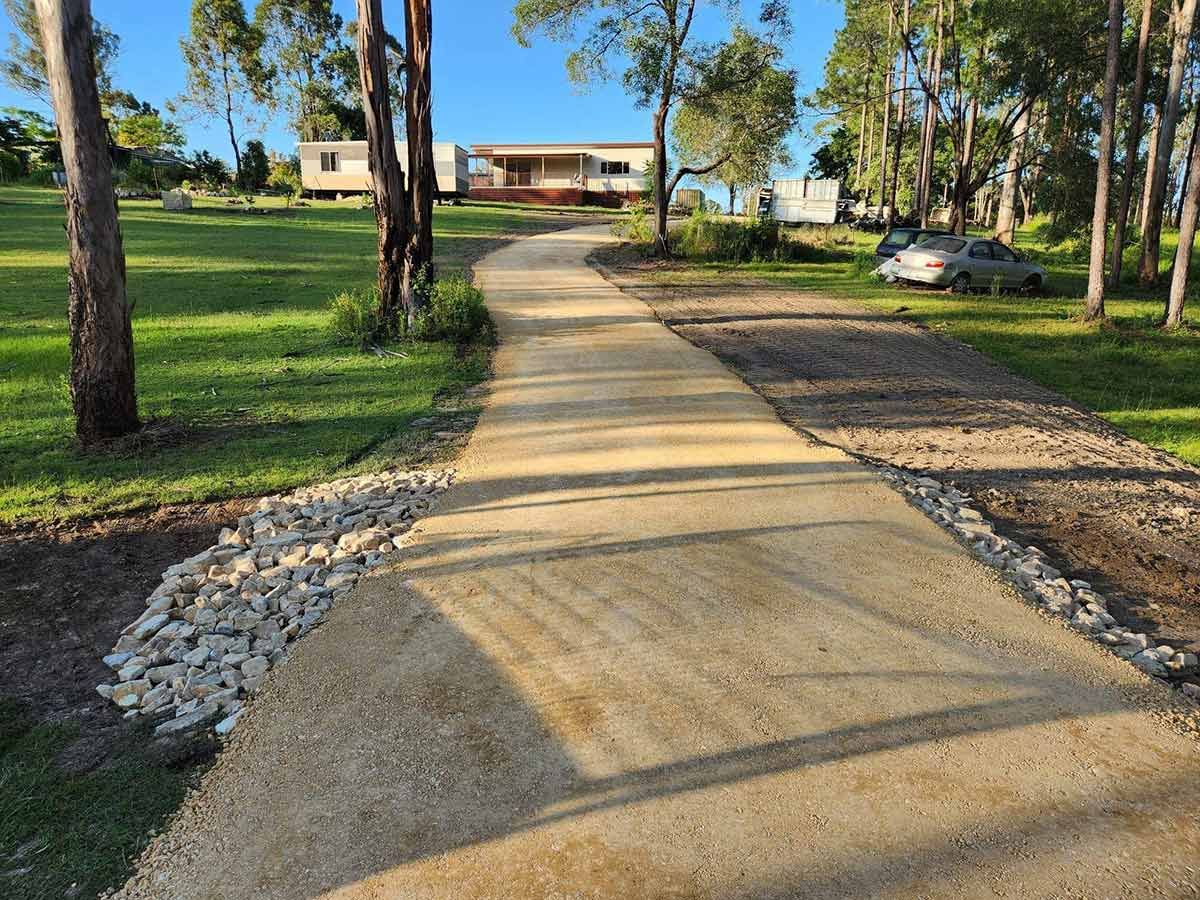 A Concrete Driveway Leading to A House Surrounded by Trees and Grass — CK's Milling & Earthworks in Tiaro, QLD
