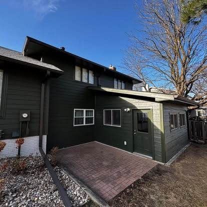 The back of a house with a green siding and a brick patio.