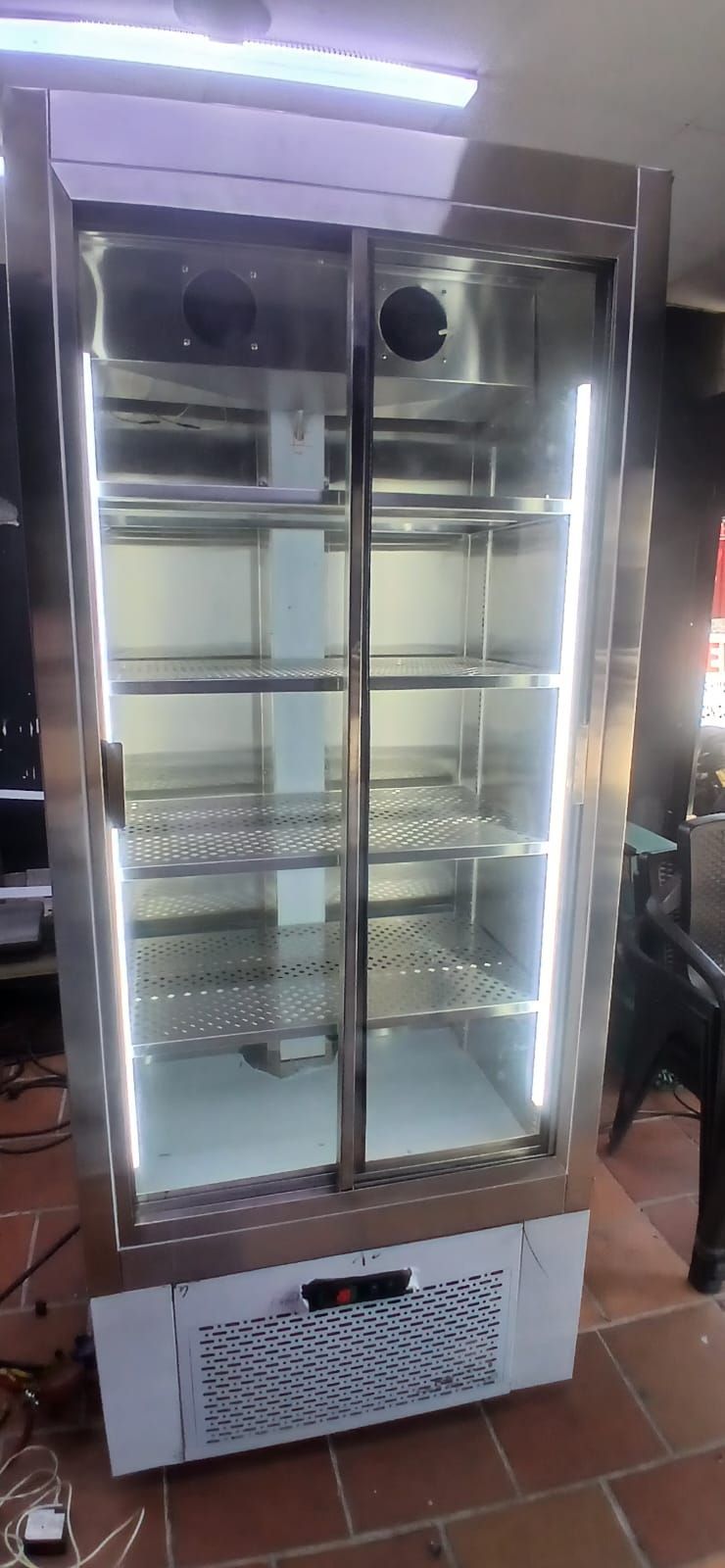 Refrigerador con vitrina de cristal y estantes metálicos en un espacio interior alicatado.