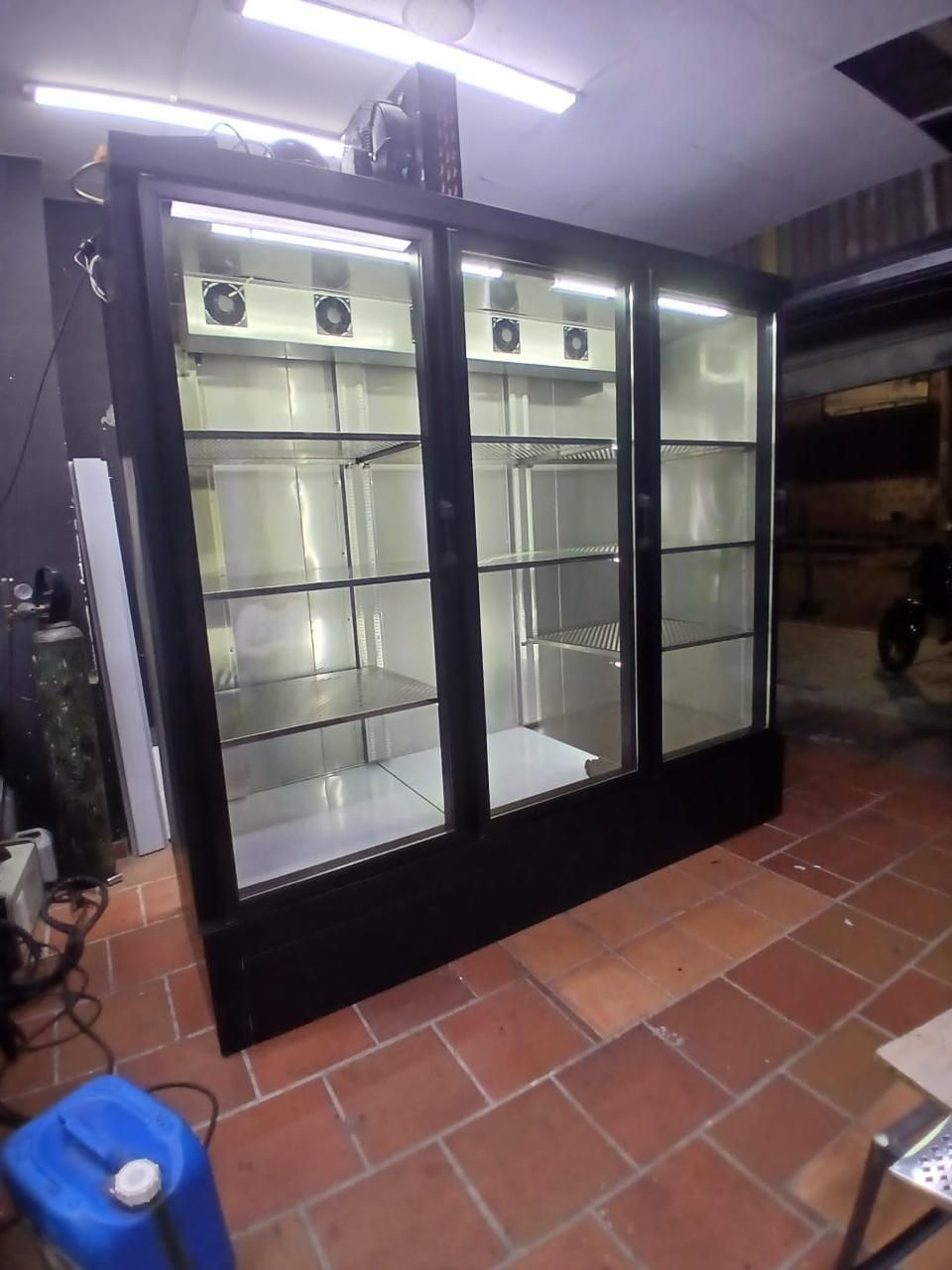Vitrina refrigerada comercial con puerta de cristal en una habitación alicatada, iluminada desde arriba