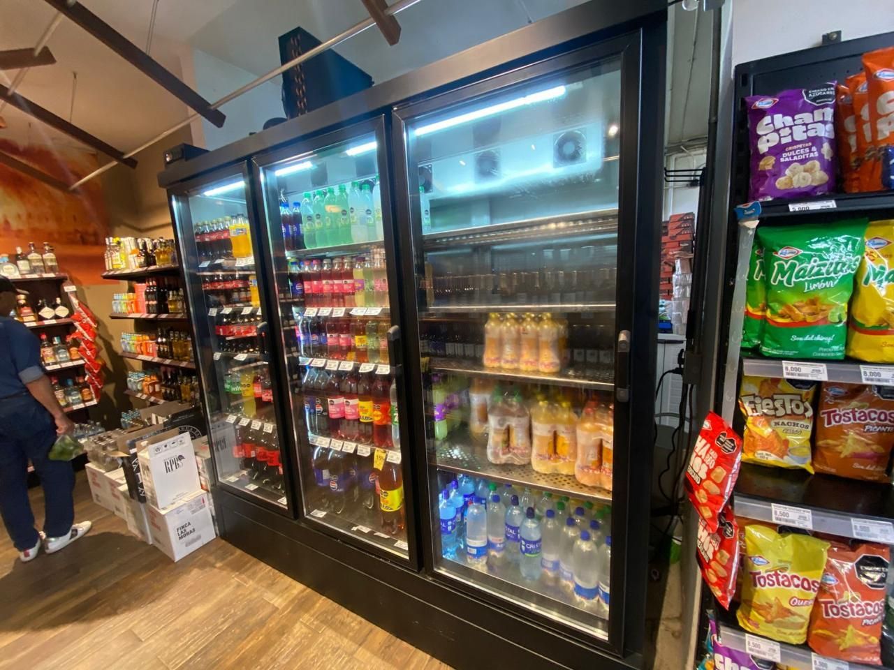 Pasillo de supermercado con refrigeradores de puertas de vidrio repletos de bebidas y aperitivos
