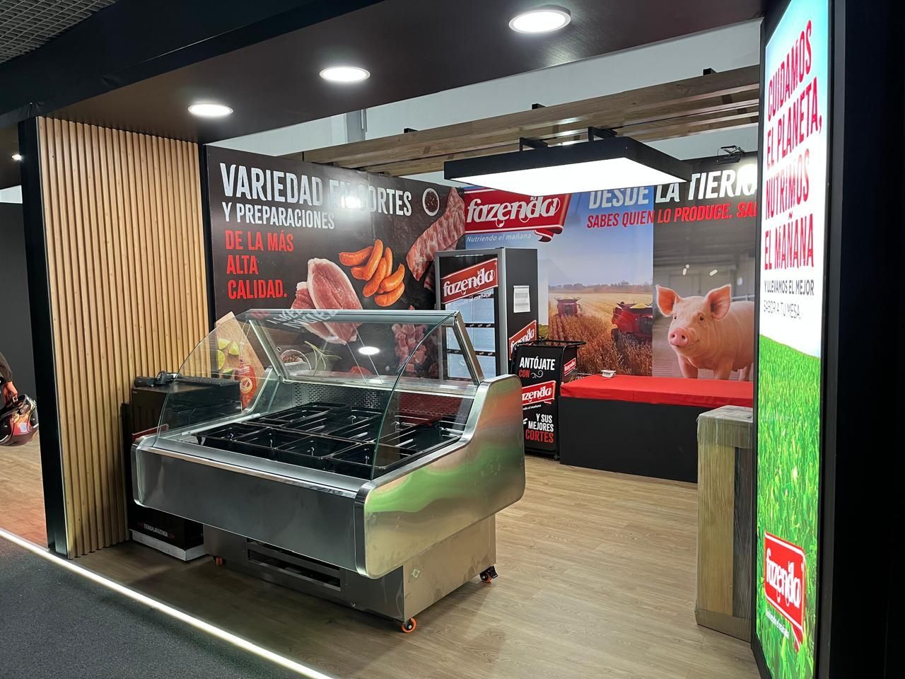 Mostrador de exhibición de carne de restaurante con letrero negro, detalles en rojo y una pared con patrón de madera.