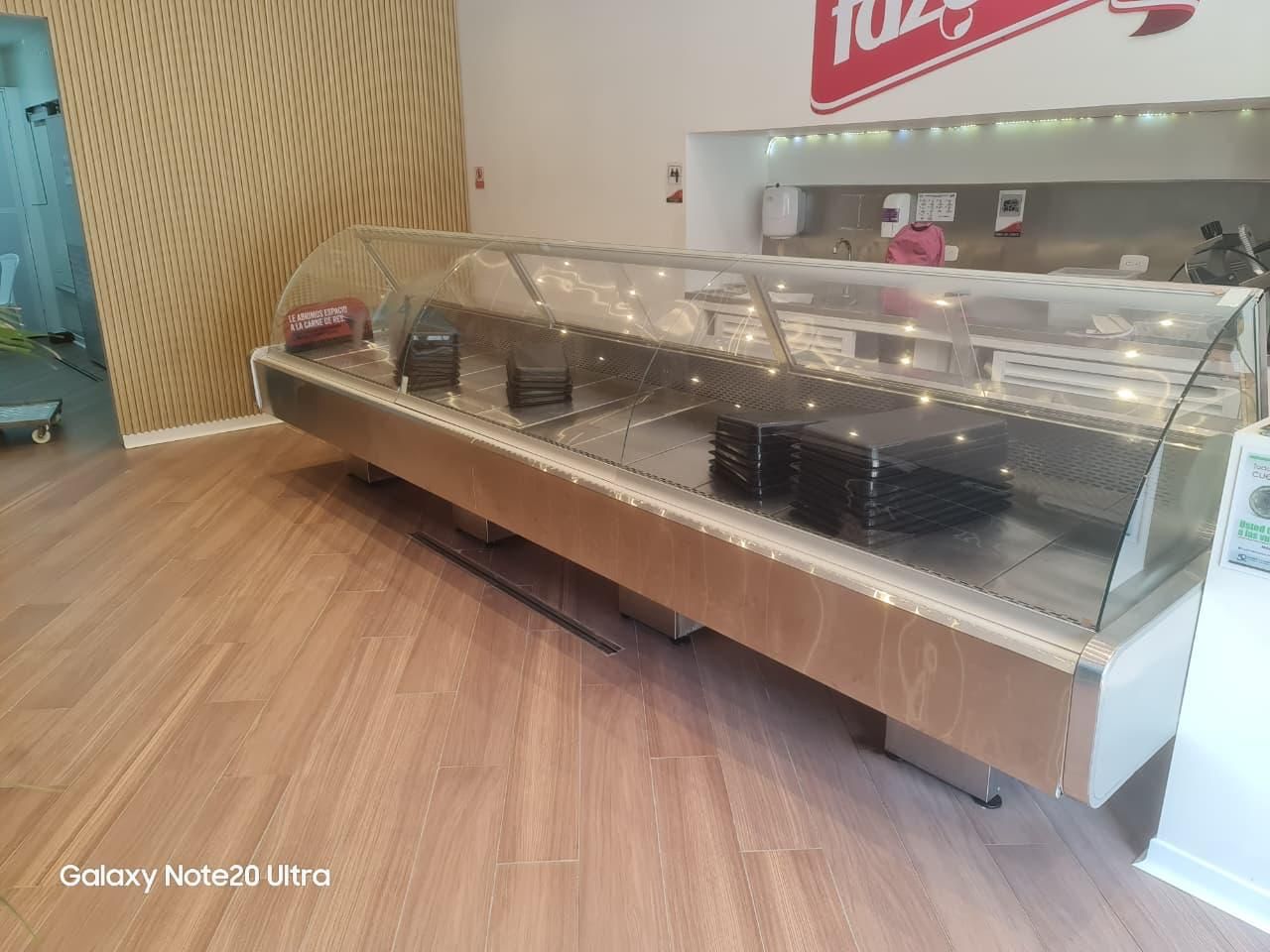 Vitrina vacía de panadería con cristal transparente, bandejas negras y suelo de madera en el interior de una tienda.