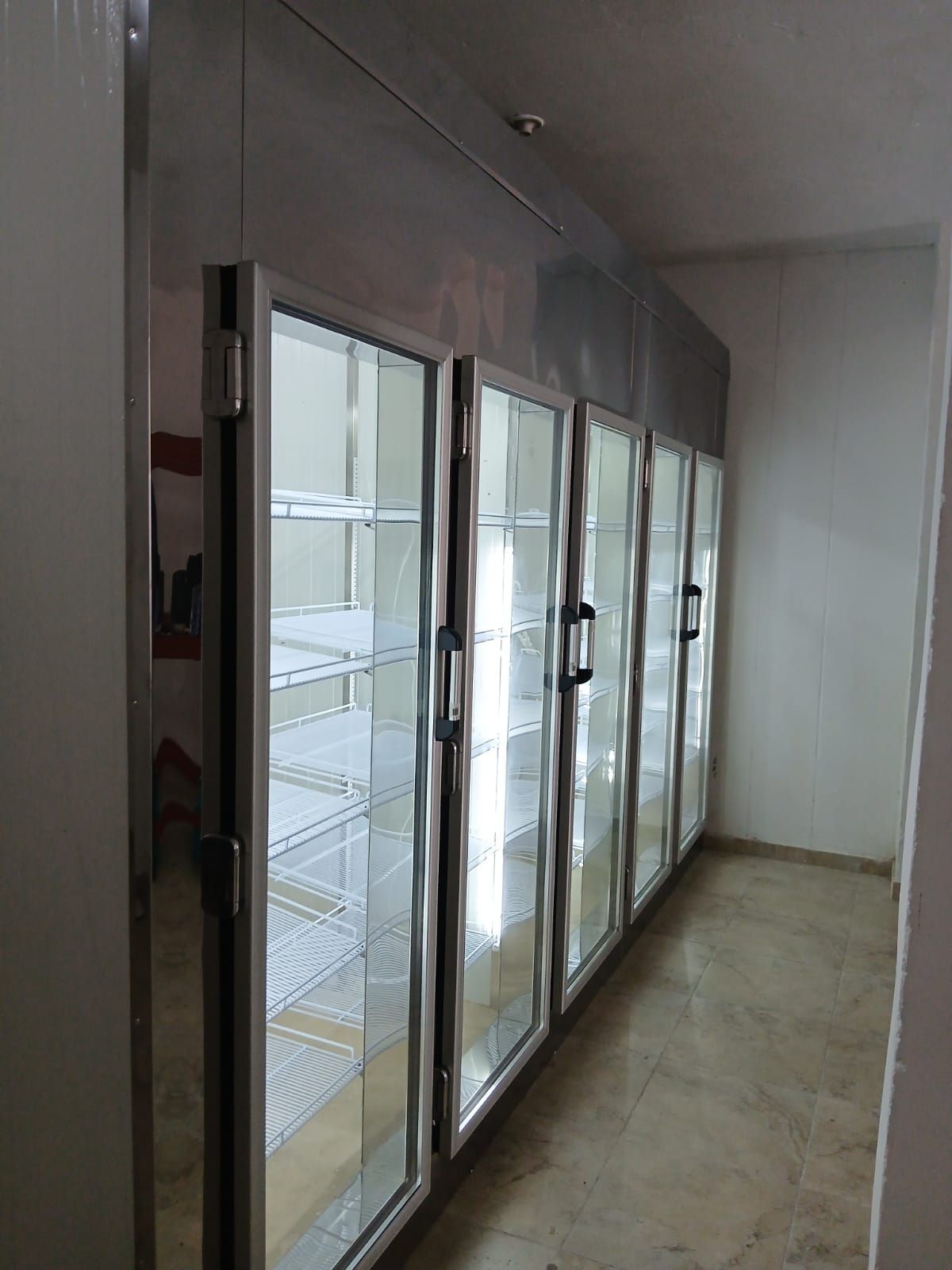 Pasillo vacío con refrigeradores con puerta de vidrio a lo largo de una pared y piso de baldosas.