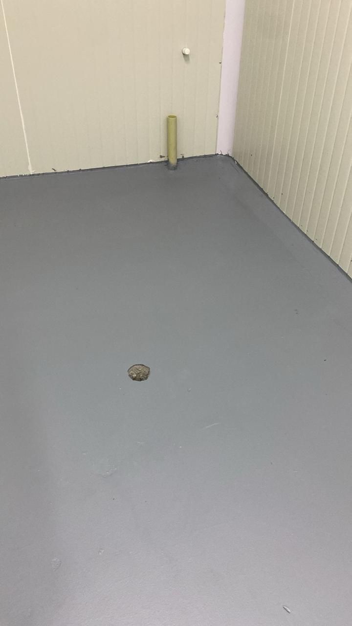 Rincón gris vacío con un pequeño desagüe en el suelo y una tubería beige contra paredes a rayas.