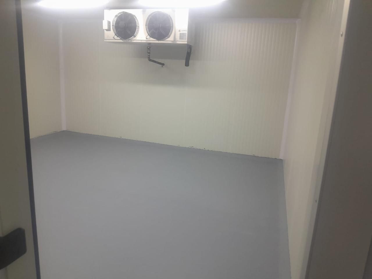 Habitación vacía con suelo gris, paredes beige y un aire acondicionado montado en la pared cerca del techo.