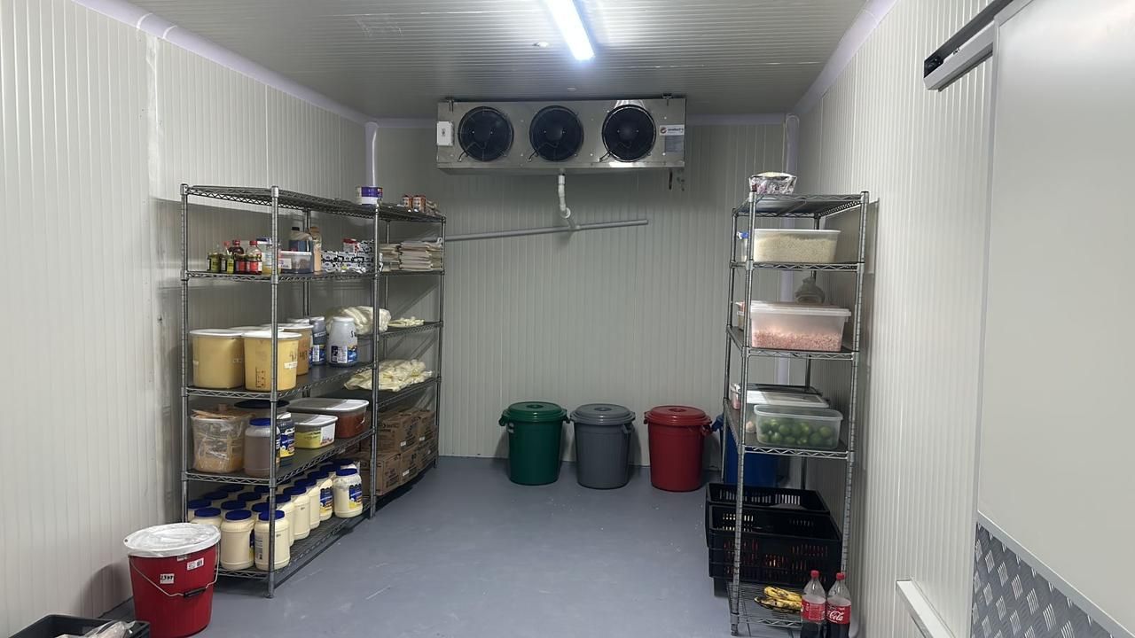 Cámara frigorífica industrial con acceso directo, equipada con estantes metálicos, cajas, contenedores