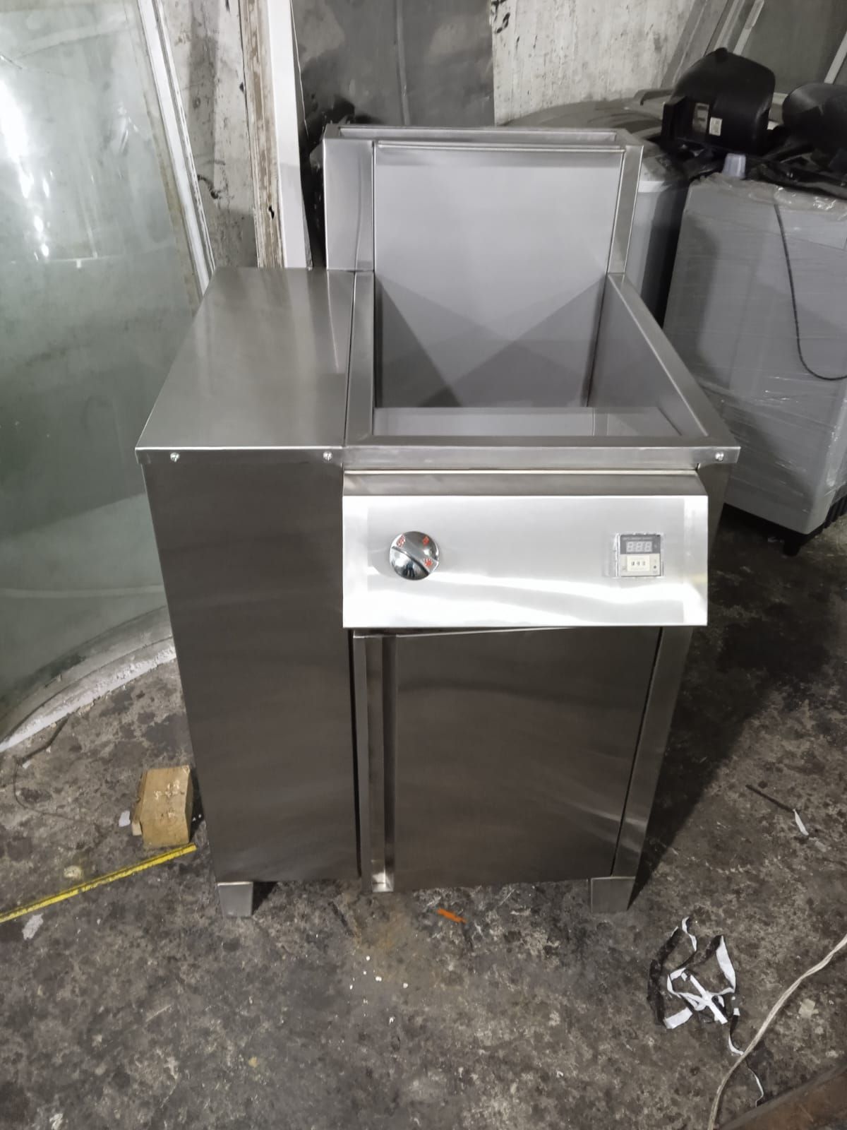 Electrodoméstico de cocina comercial de acero inoxidable con parte superior abierta y panel de control frontal en un taller.