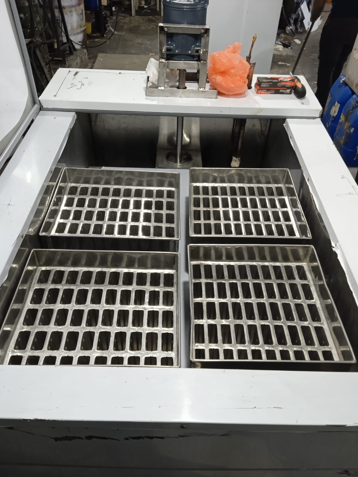Máquina industrial con cuatro bandejas de rejilla metálica dentro de una carcasa con marco blanco.