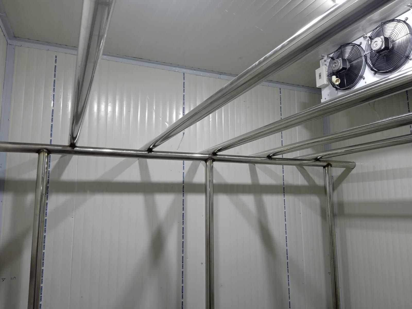 Trastero vacío con estructura metálica blanca, rieles superiores y ventilador de pared.