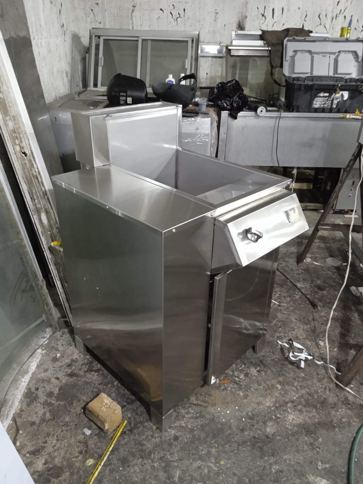 Máquina industrial de acero inoxidable en un taller, con la parte superior inclinada y un panel frontal tipo cajón.