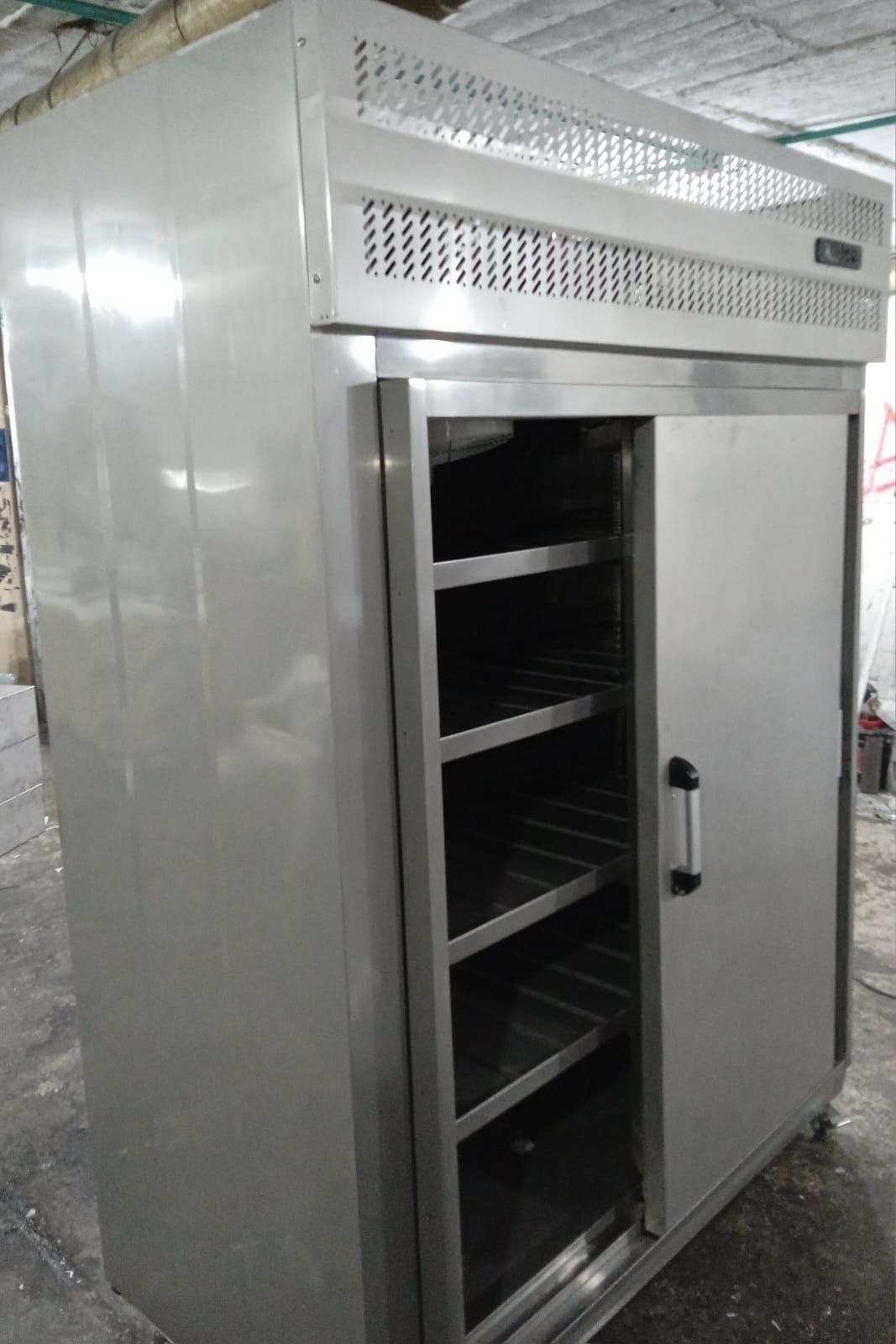 Armario comercial de acero inoxidable con la puerta abierta y los estantes vacíos en una cocina industrial.