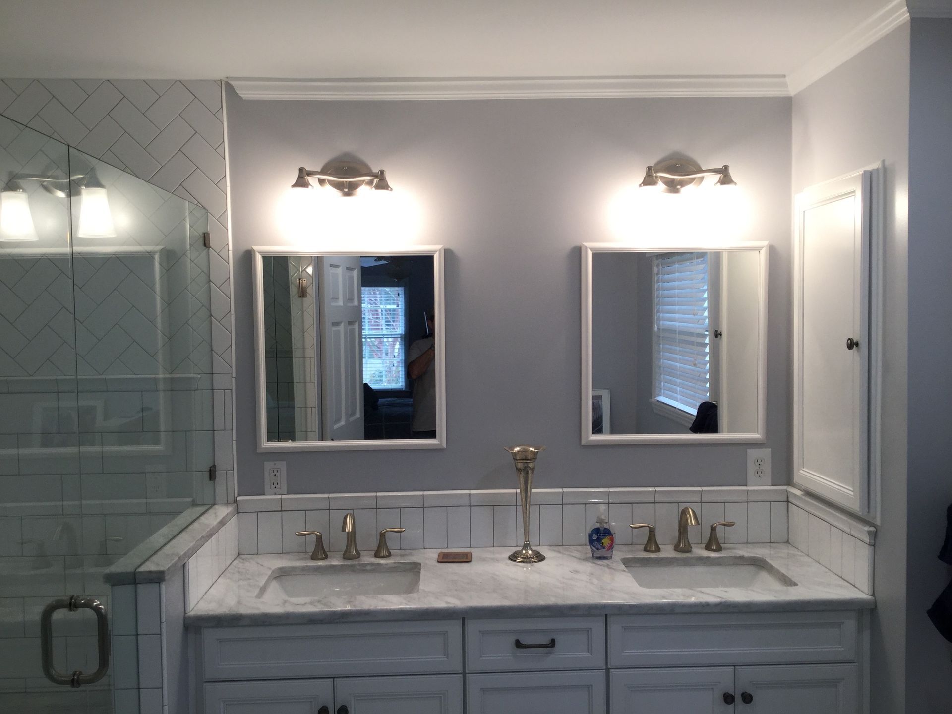 Bright white bathroom vanity with double sinks, mirrors, wall sconces, and glass shower.