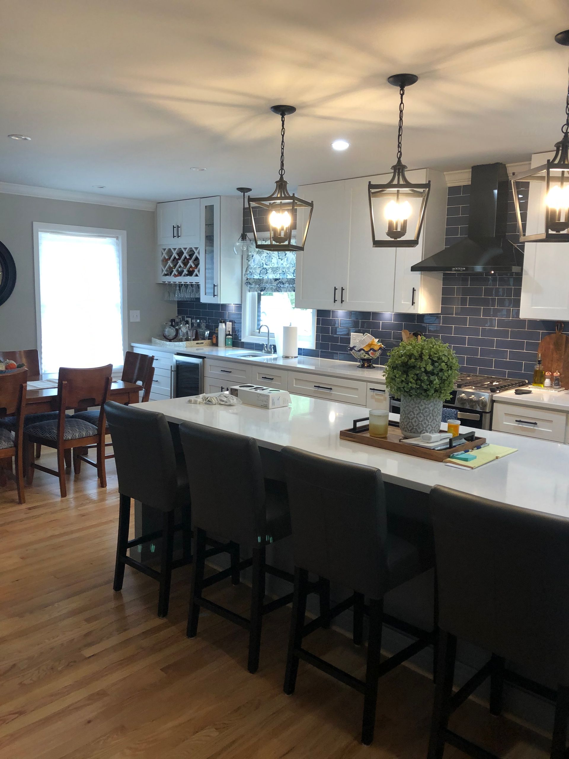 Modern kitchen with white island, dark barstools, pendant lights, and blue tile backsplash