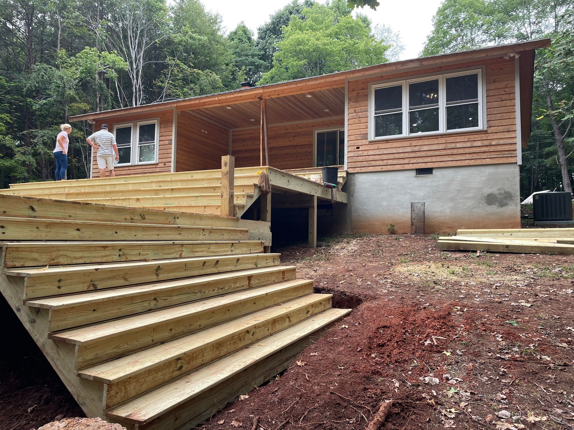 Wooden stairs and ramp leading to a brick house under construction, with workers on the porch.