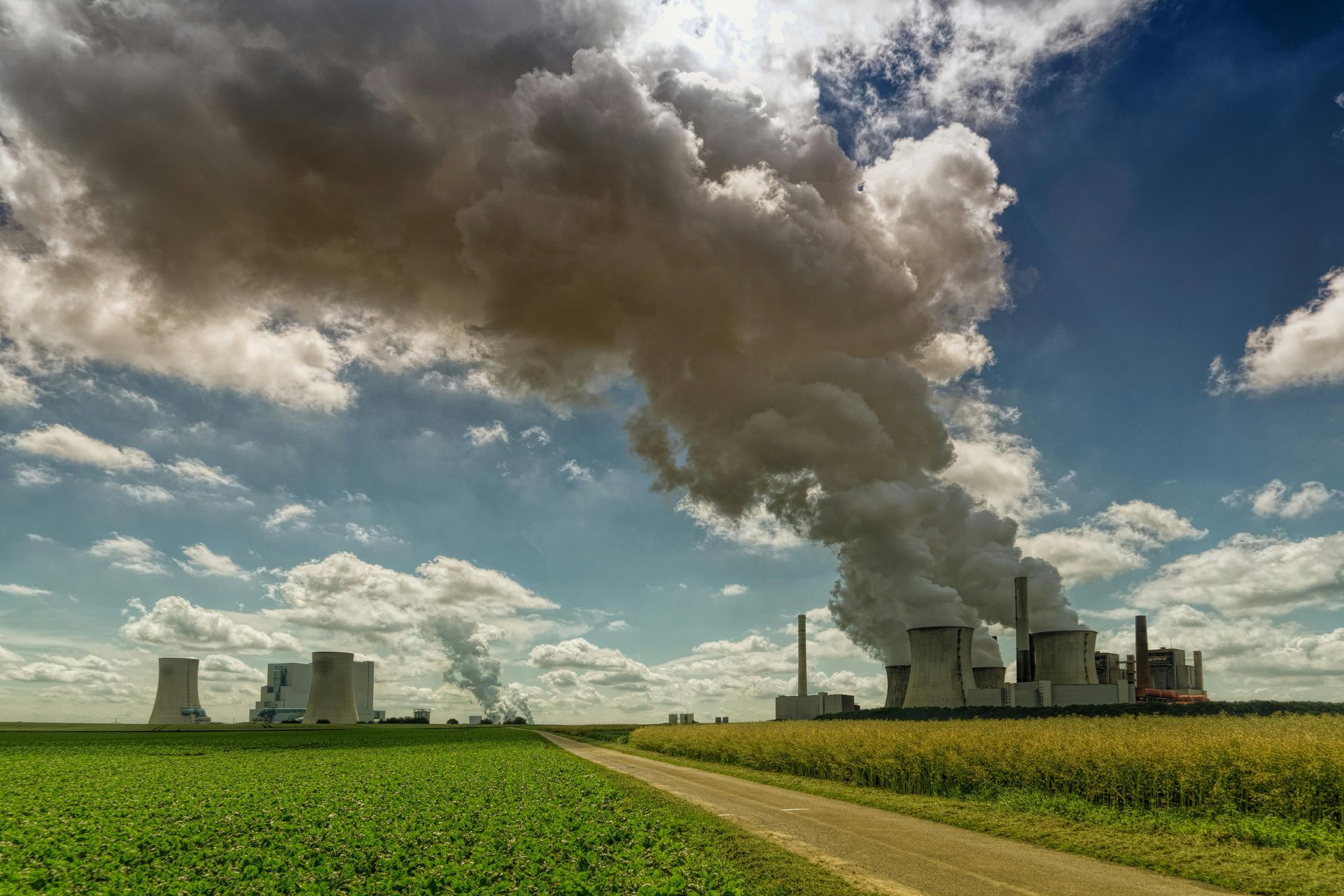 Industrial power plant with smoke stacks beside a green field under a cloudy sky