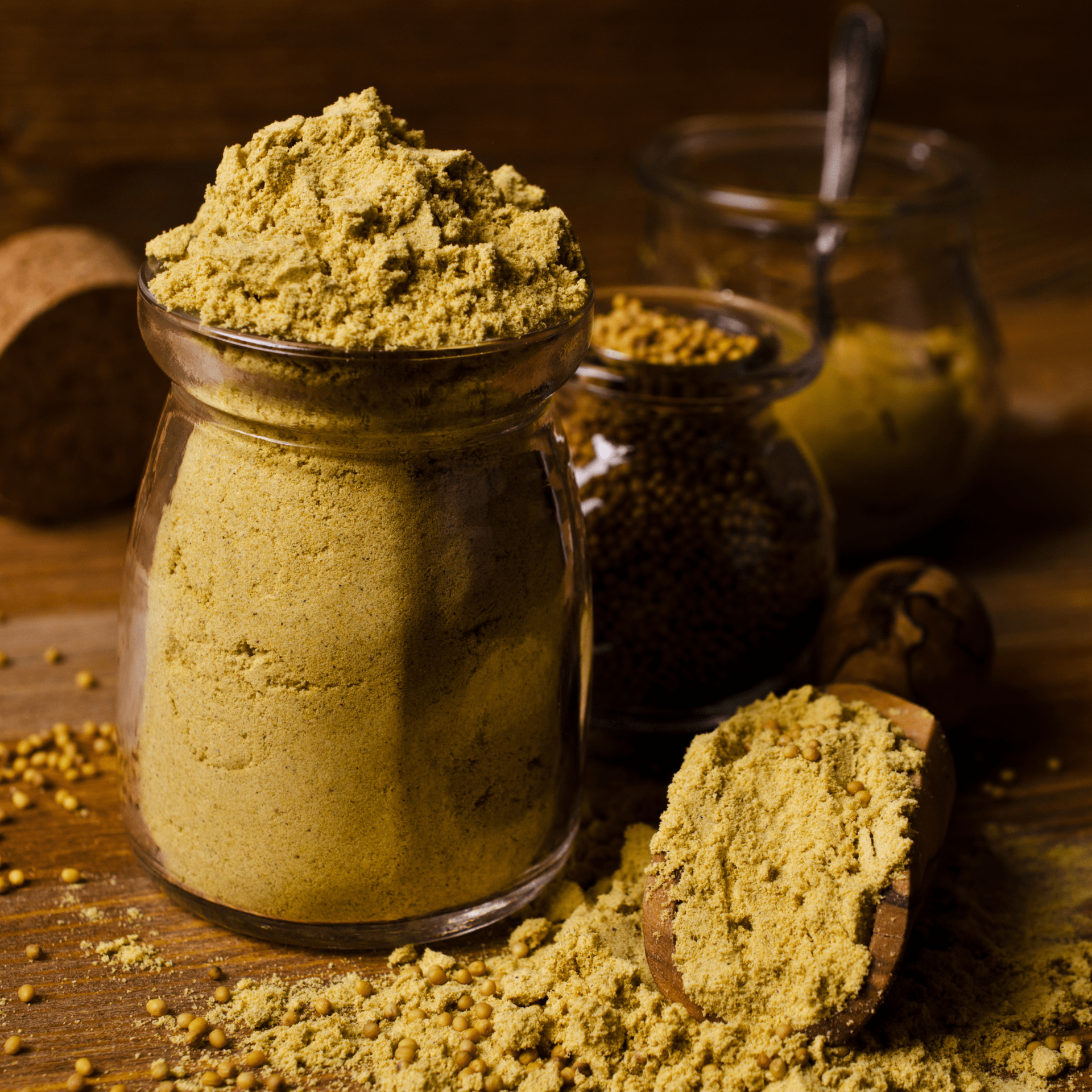 Mustard powder in a glass jar, spoon, and scattered on a wooden surface.