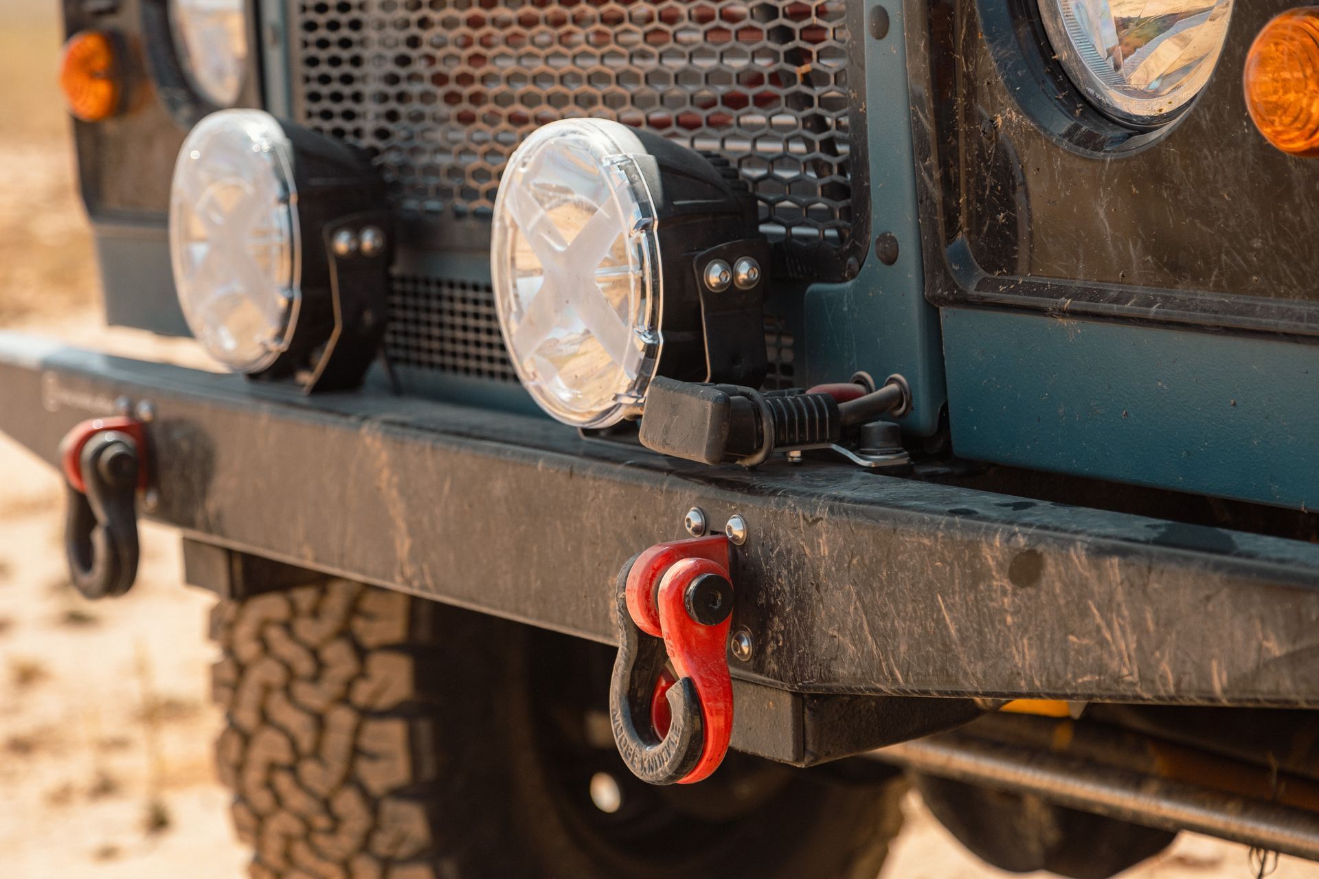 Close-up of a dark green off-road vehicle's front bumper with tow hooks and auxiliary lights.