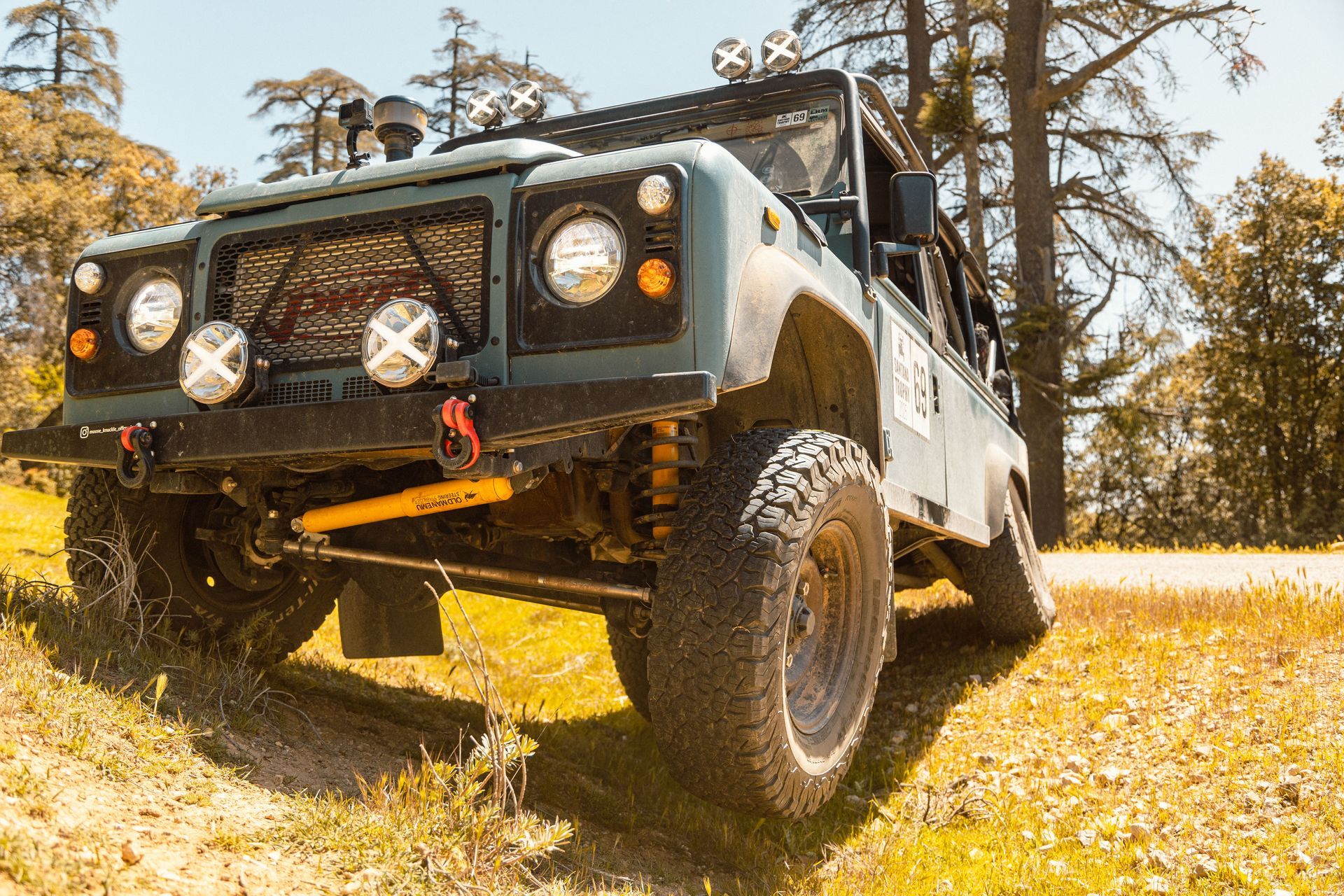 Blue off-road SUV on a grassy hill, showcasing its rugged modifications against a backdrop of trees.