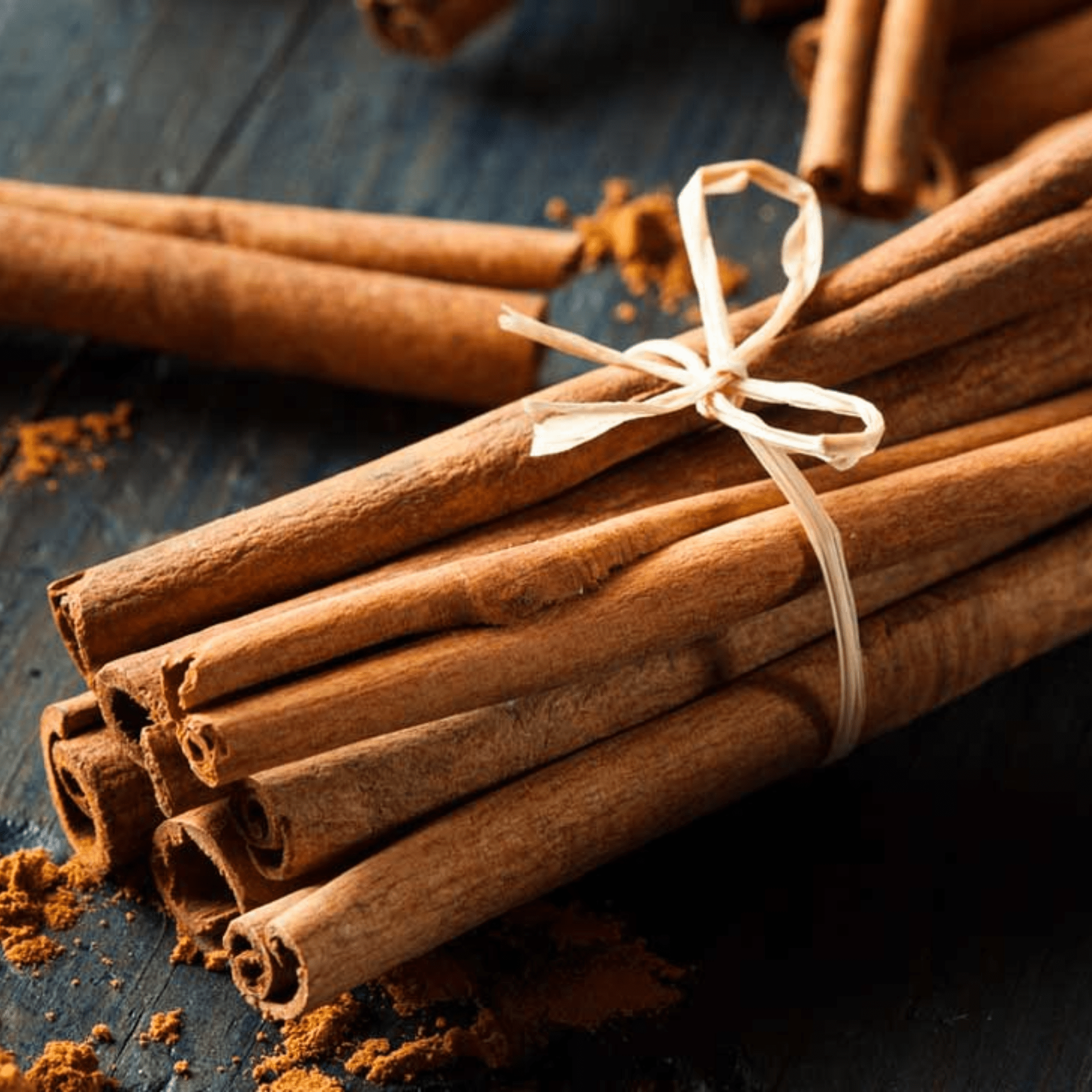 Bundle of cinnamon sticks tied with twine on a blue surface.