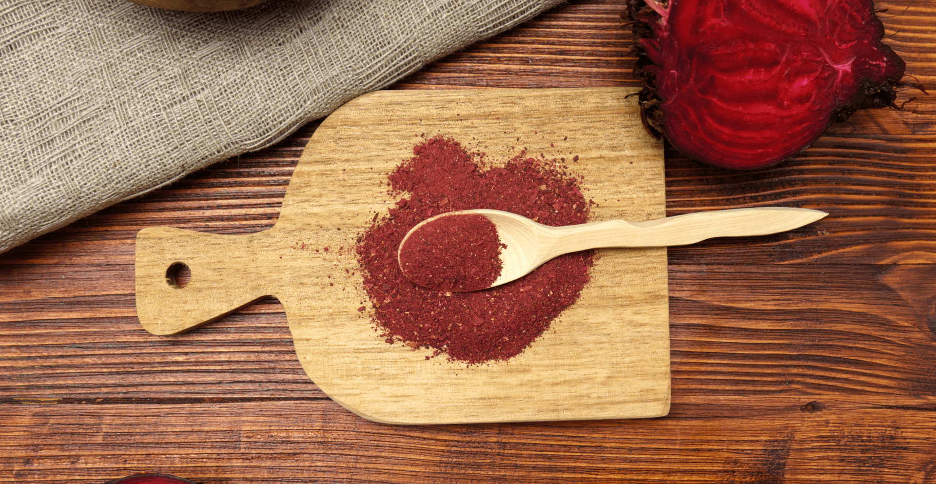 Beetroot powder on a wooden board with a spoon, alongside a red beet.