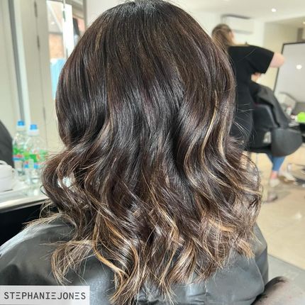 Wavy dark brown hair with caramel highlights in a salon setting