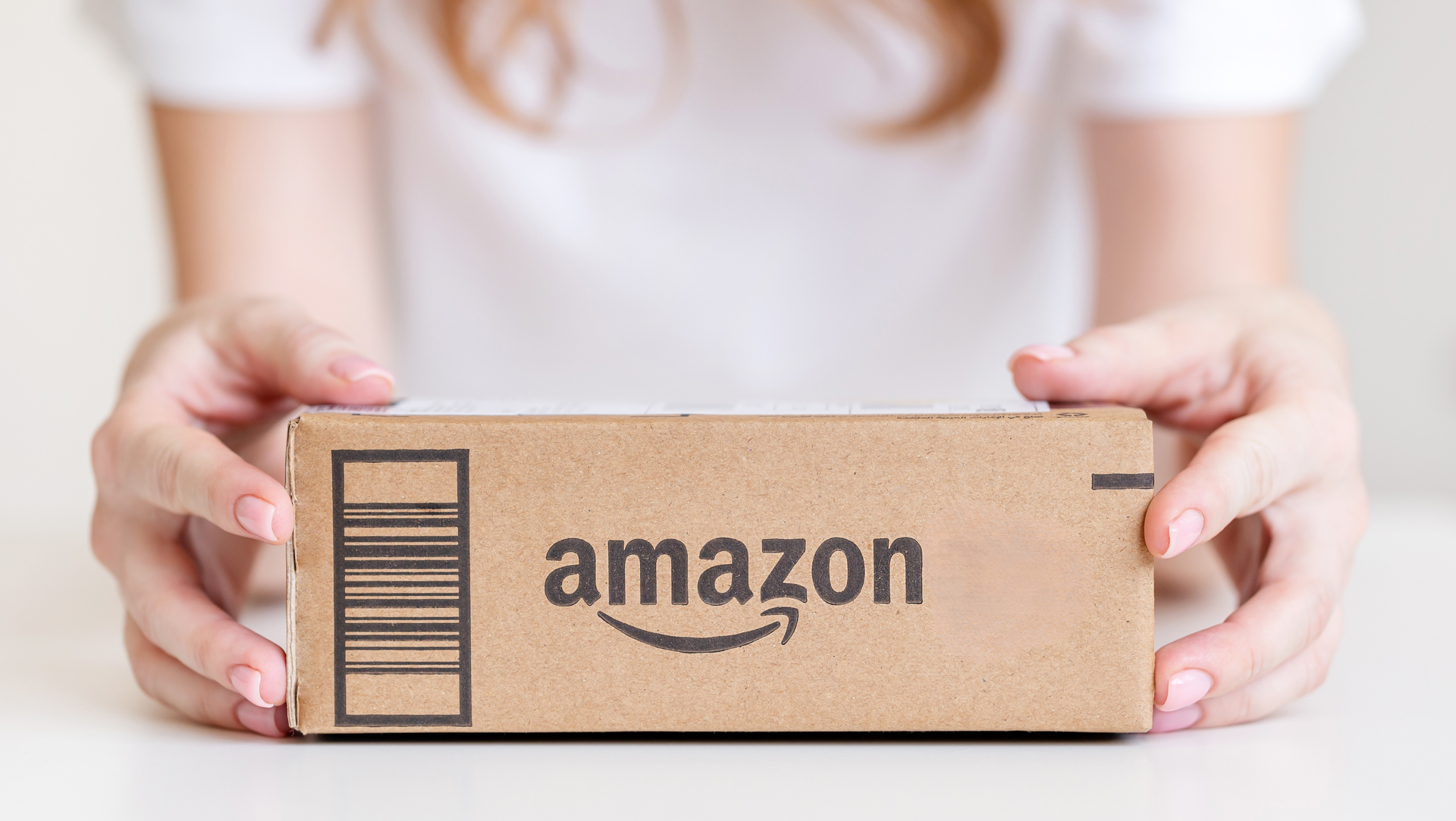 Person holding an Amazon shipping box with the Amazon logo visible.
