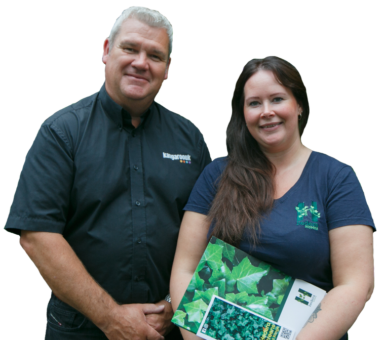 A man and woman smiling at the camera; the woman holds a brochure with green plants on it.